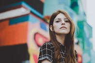 Portrait of a fashionable woman with glasses posing confidently outdoors in front of a vibrant mural.